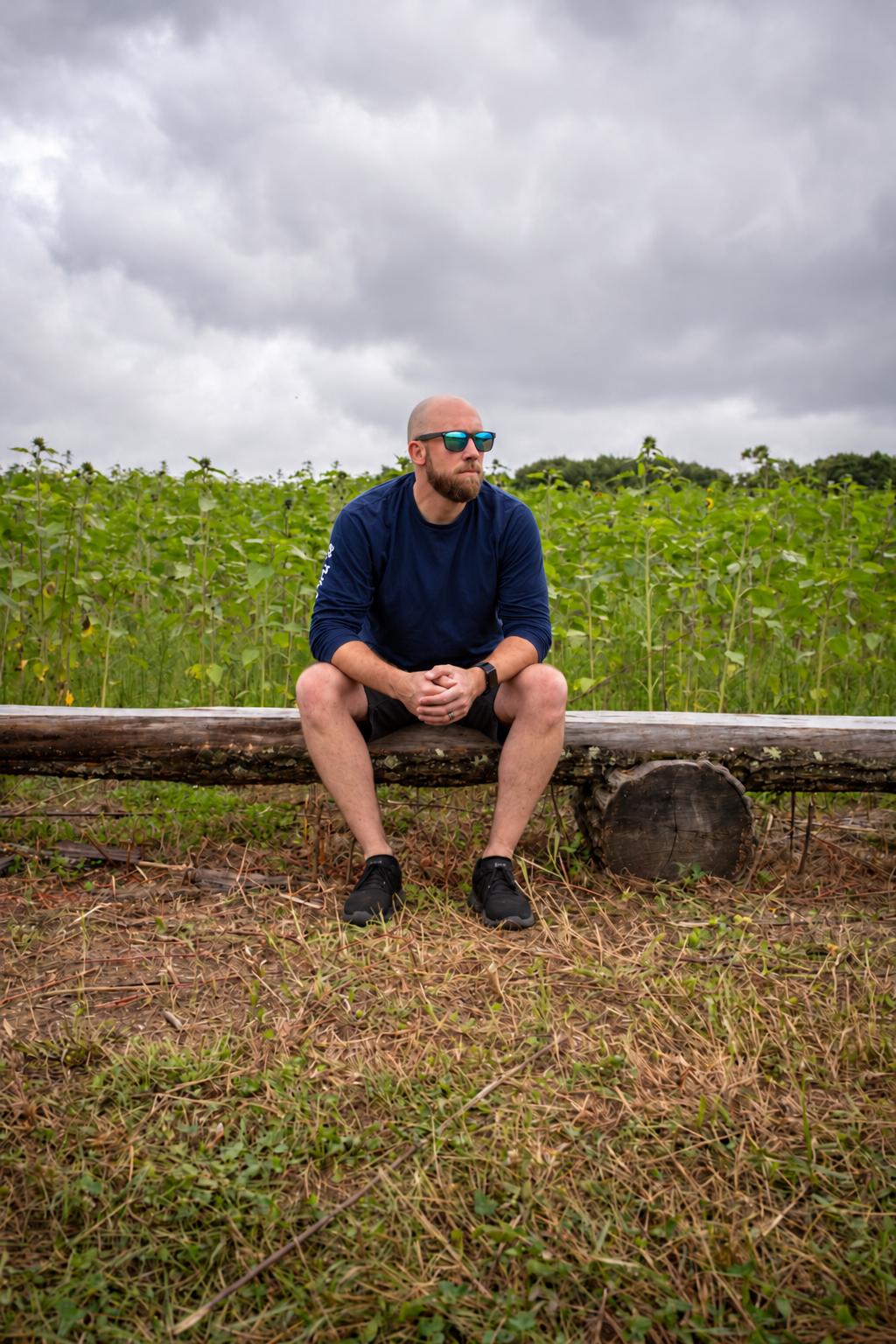 Craig Rivest seated on a log in an open field beneath a cloudy sky